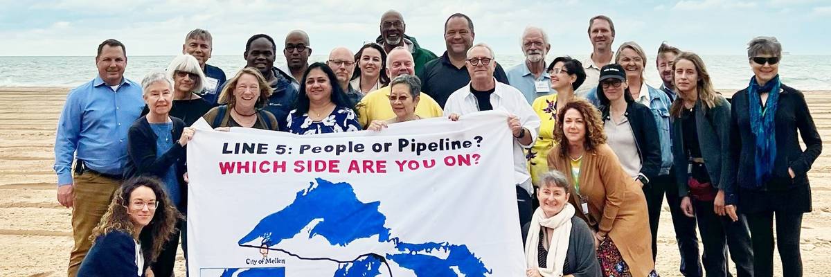 Activists gather around a sign reading, "Line 5: people or pipeline? Which side are you on?"