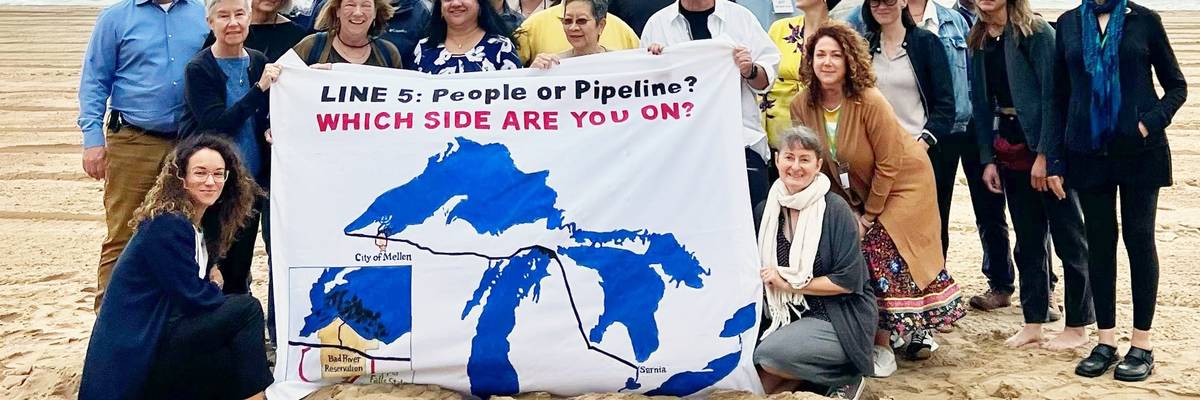 Activists gather around a sign reading, "Line 5: people or pipeline? Which side are you on?"