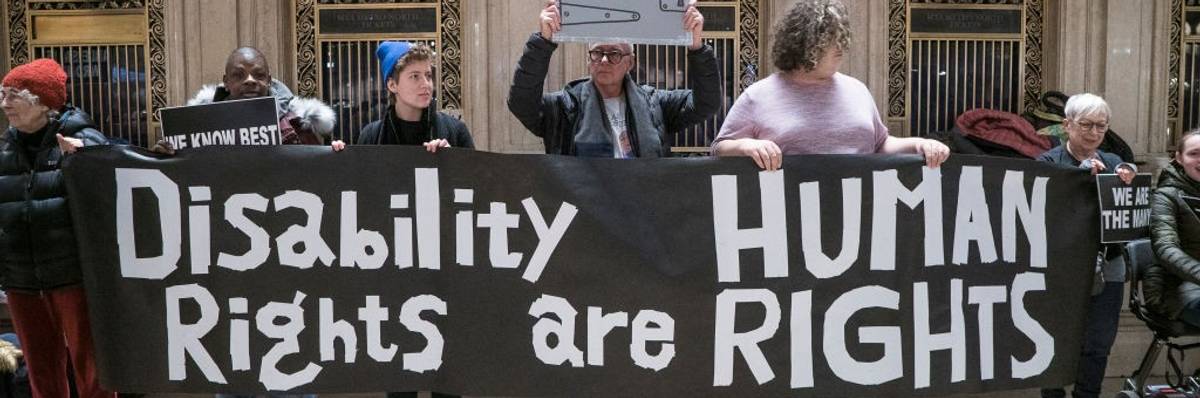 Activists hold a black banner that reads “Disability Rights are Human Rights” in white writing.