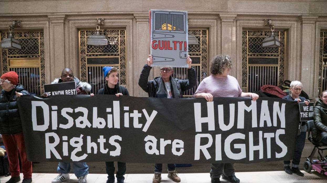 Activists hold a black banner that reads “Disability Rights are Human Rights” in white writing.