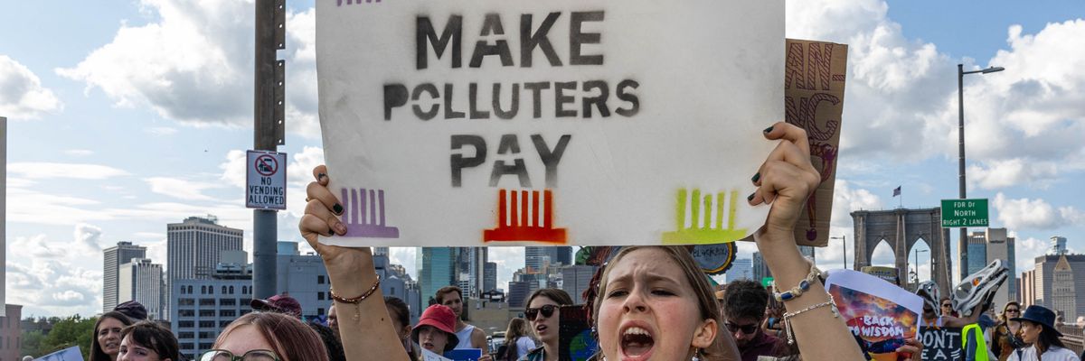 Activists hold signs reading, "Make Polluters Pay" as they cross the Brooklyn Bridge