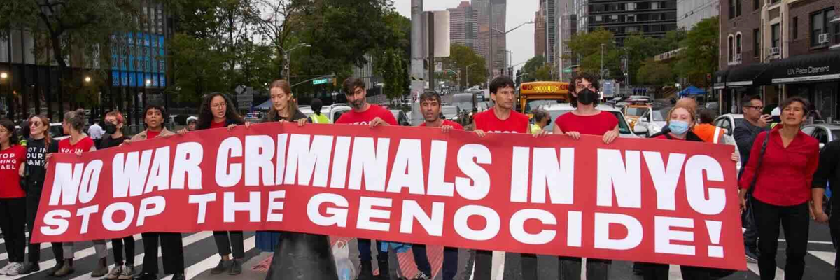 Activists in red t-shirts carry a banner reading, "No war criminals in NYC. Stop the Genocide!"