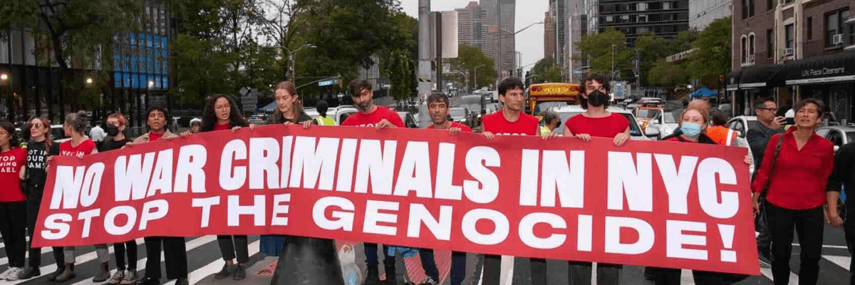 Activists in red t-shirts carry a banner reading, "No war criminals in NYC. Stop the Genocide!"