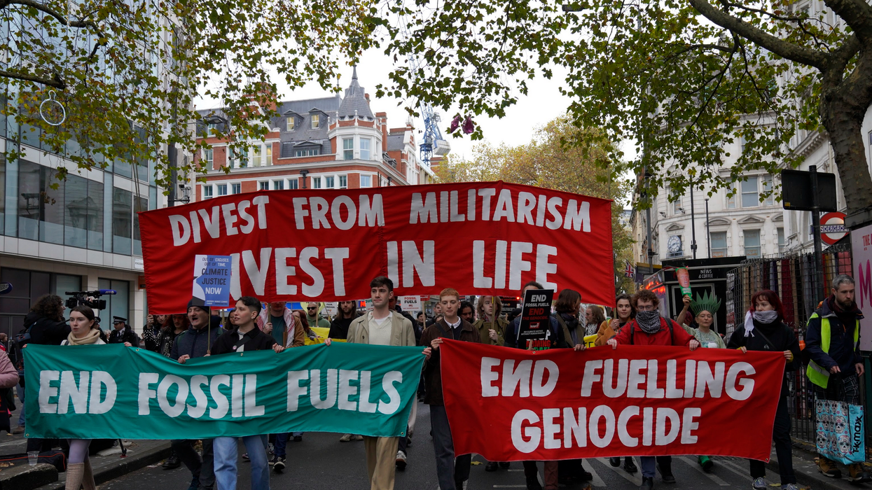 Activists march in London with banners reading, "Divest from militarism, invest in life," "end fossil fuels," and "end fueling genocide."
