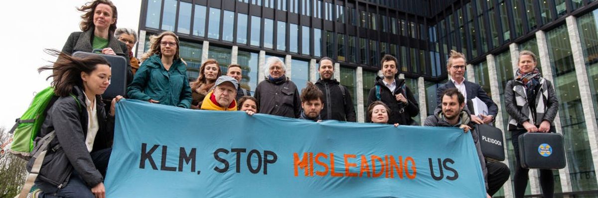 Activists stand around a blue sign reading, "KLM, Stop Misleading Us."
