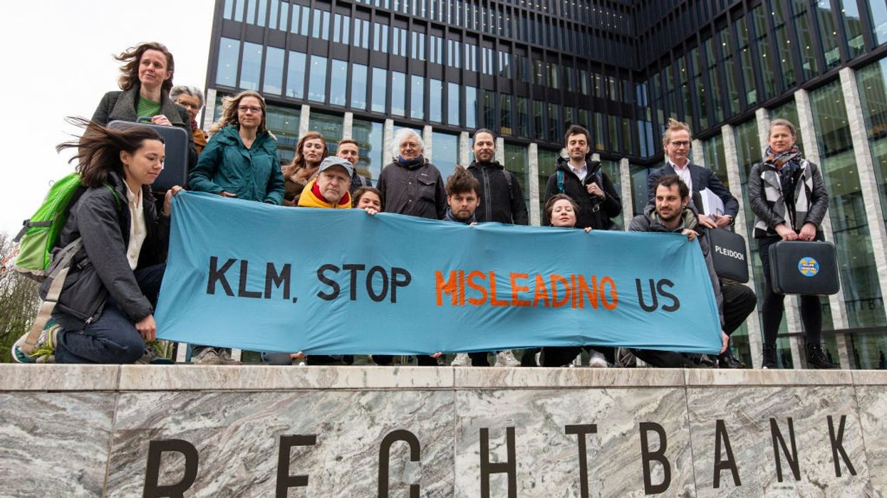 Activists stand around a blue sign reading, "KLM, Stop Misleading Us."