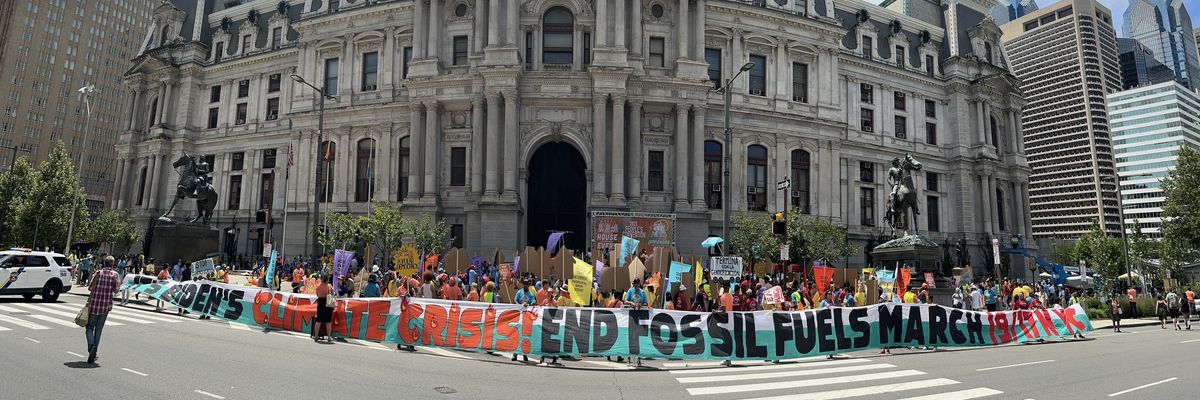 Activists stand in front of a building with a banner reading, "It's Biden's Climate Crisis! End Fossil Fuels March 9/17 NYC."