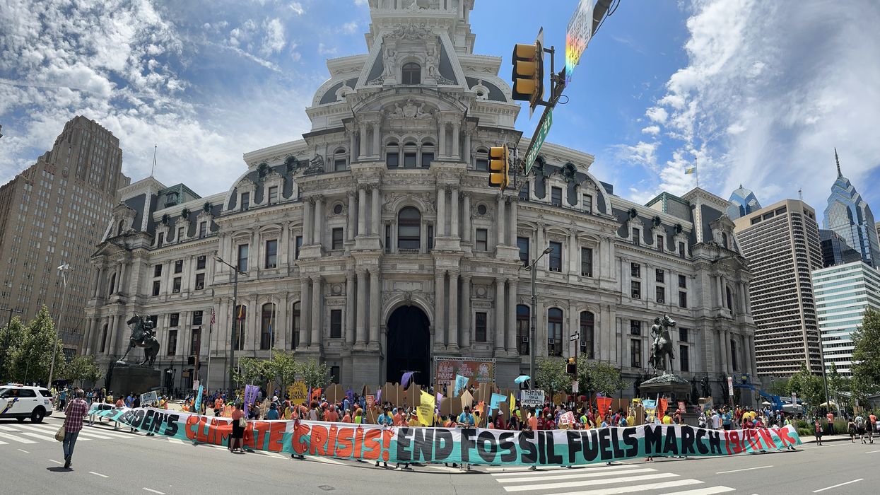 Activists stand in front of a building with a banner reading, "It's Biden's Climate Crisis! End Fossil Fuels March 9/17 NYC."