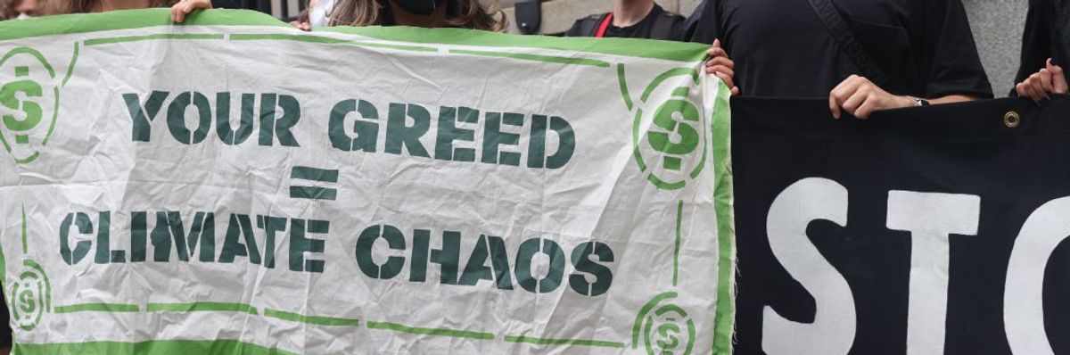 Activists stand with a sign reading, "Your greed = climate chaos."