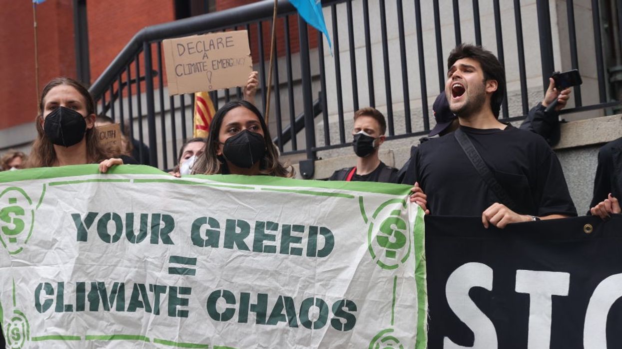 Activists stand with a sign reading, "Your greed = climate chaos."