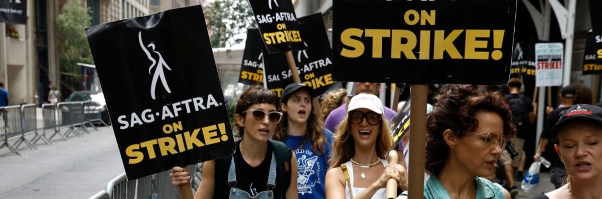 Actors picket carrying signs saying, "SAG-AFTRA on strike!"