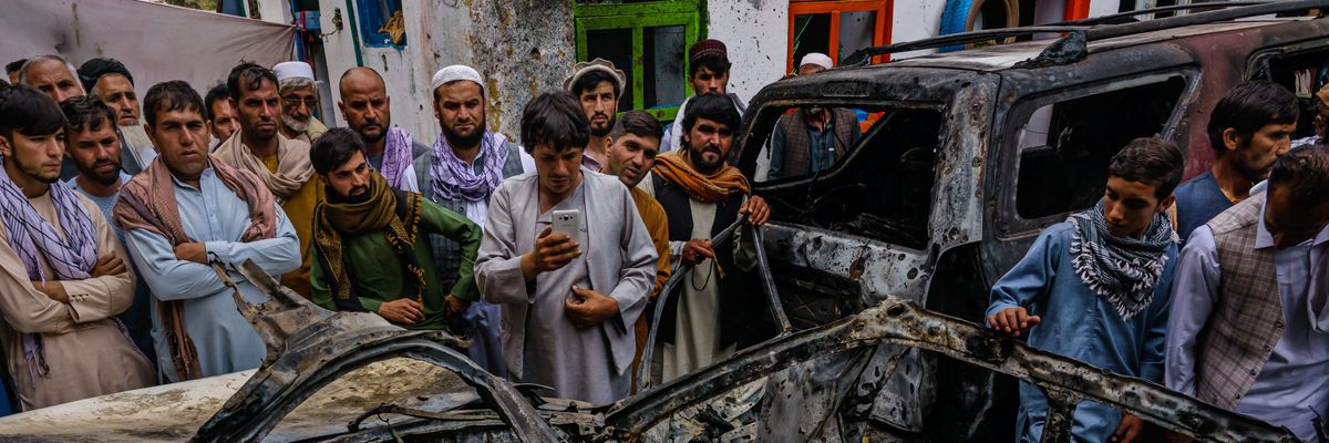 Afghans gather around a car incinerated by a U.S. drone strike