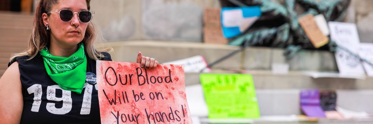 An abortion rights activist holds a sign reading, "Our blood will be on your hands"