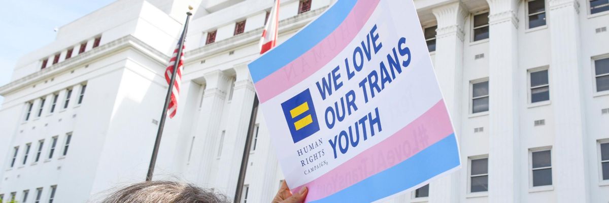 An activist holds a sign reading "We Love Our Trans Youth"