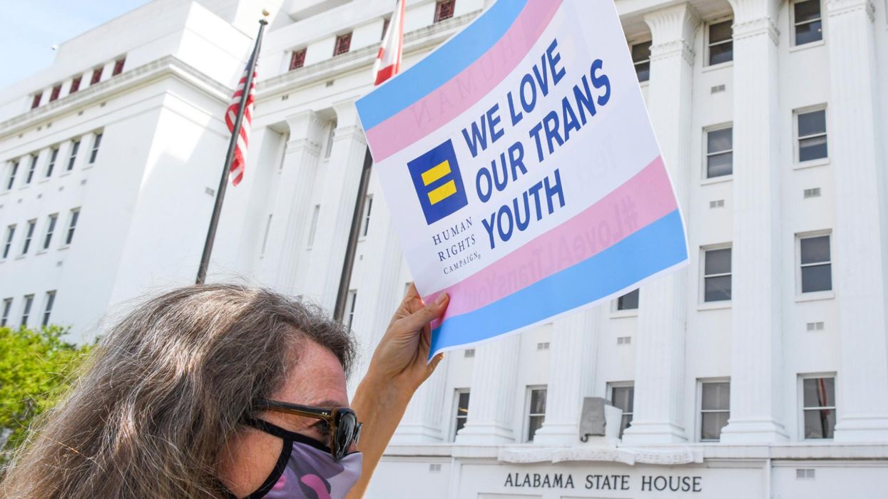 An activist holds a sign reading "We Love Our Trans Youth"
