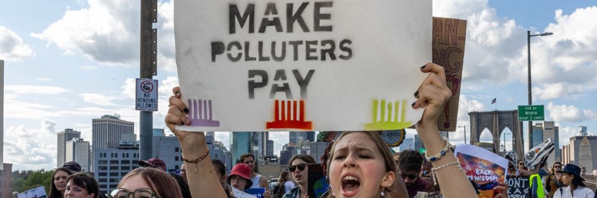 An activist holds up a sign reading, "Make Polluters Pay"