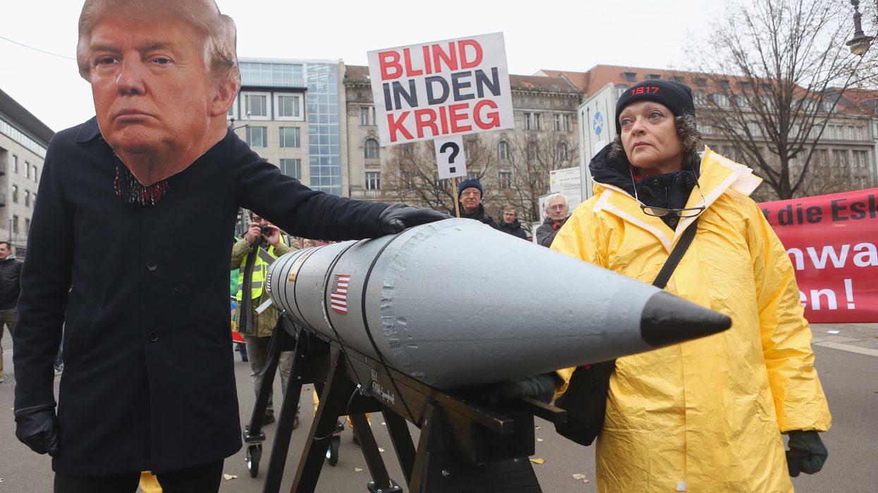 An activist in a Trump mask pats a nuclear weapon.