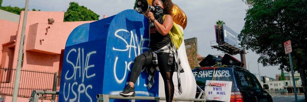 An activist stands on a mock mailbox with the message "Save USPS"
