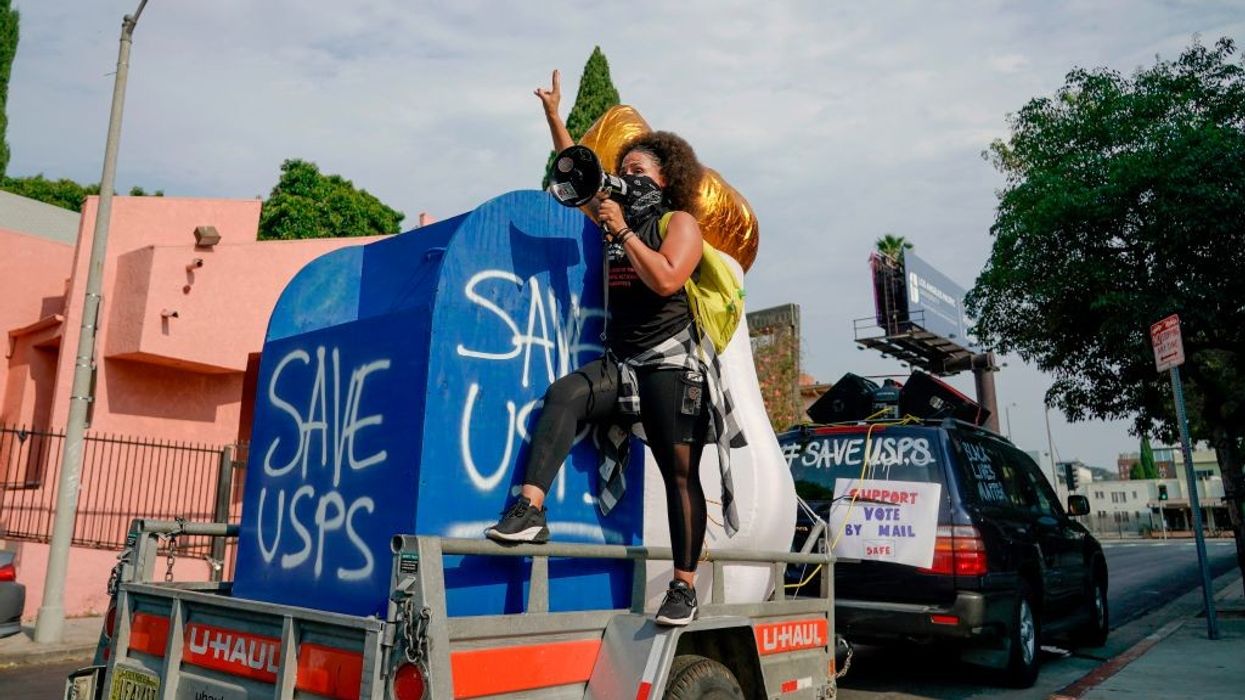 An activist stands on a mock mailbox with the message "Save USPS"