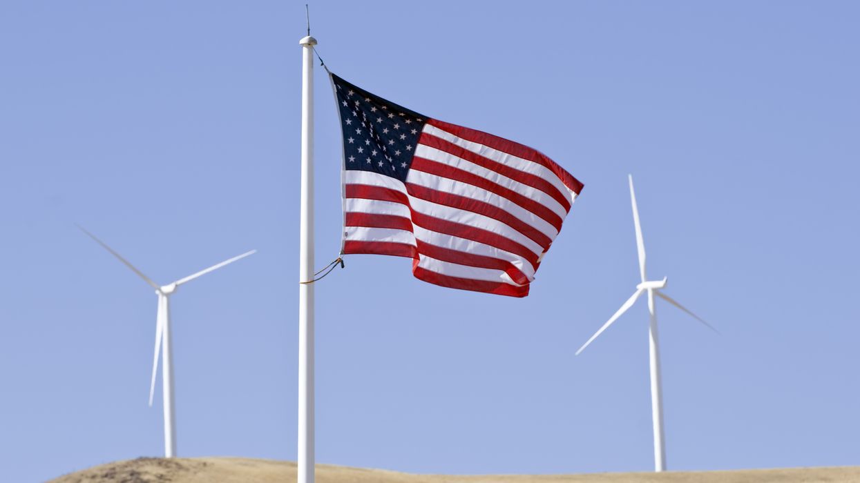 An American flag waves between two wind turbines.