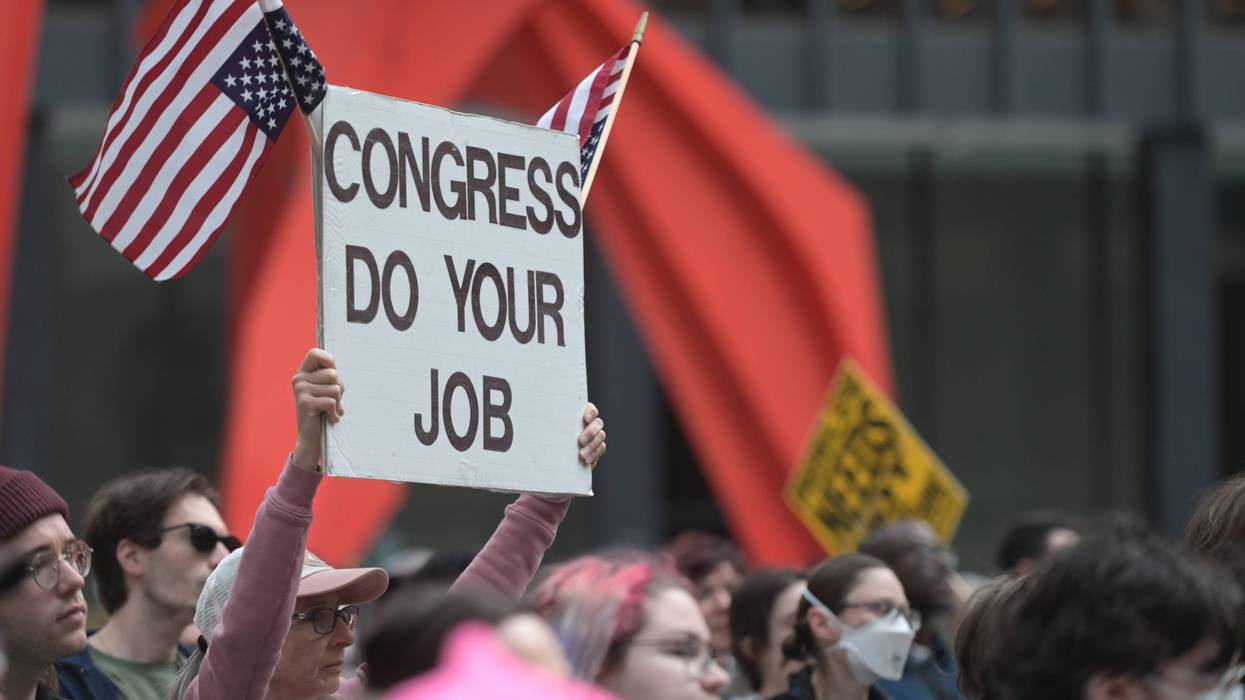 An anti-Iran War protester holds a sign with upside-down US flags reading "Congress do your job"