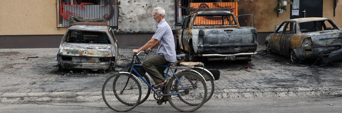 An elderly man pushes two bikes past a bomb-scarred building in Ukraine.