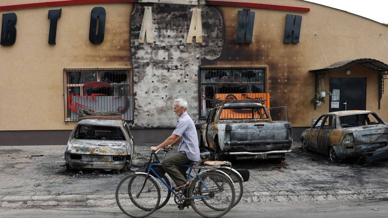 An elderly man pushes two bikes past a bomb-scarred building in Ukraine.