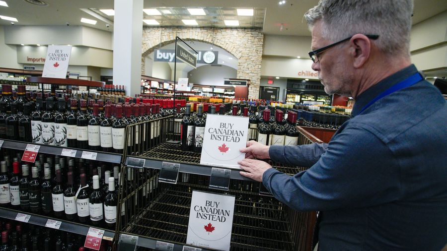 An employee places "Buy Canadian Instead" signs on a shelf at a liquor store