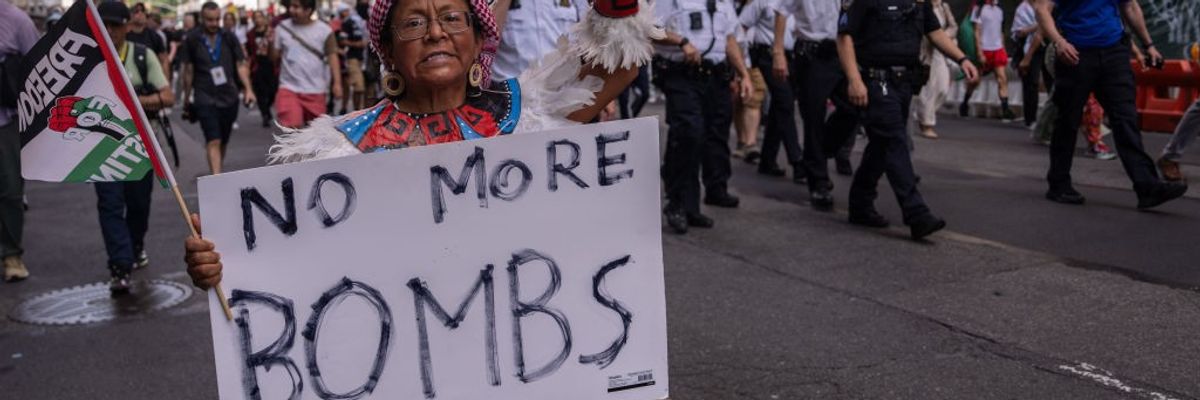An Indigenous woman marches with a "Freedom for Palestine" flag and a sign reading "No More Bombs"
