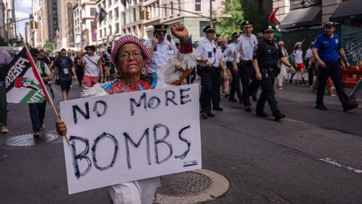 An Indigenous woman marches with a "Freedom for Palestine" flag and a sign reading "No More Bombs"