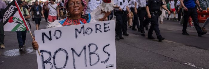 An Indigenous woman marches with a "Freedom for Palestine" flag and a sign reading "No More Bombs"