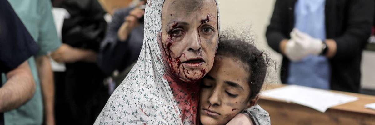 An injured Palestinian woman covered in blood hugs an injured girl after an Israeli bombing