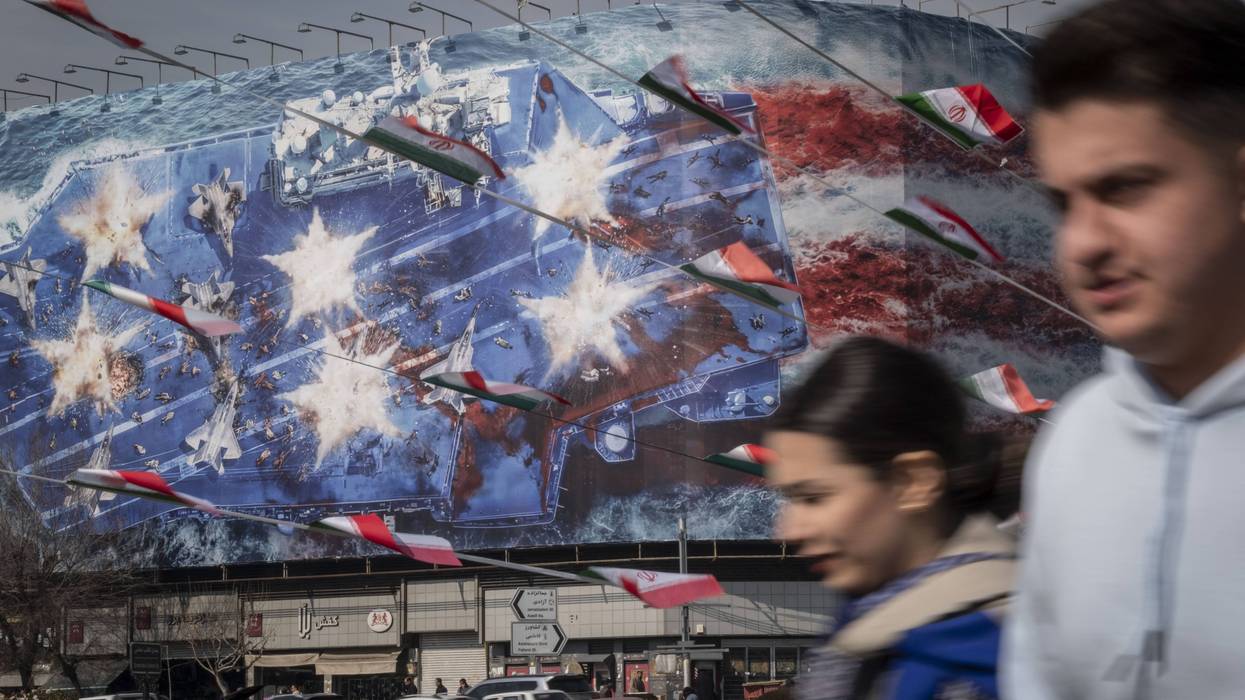 An Iranian man and women walk by an anti-American mural