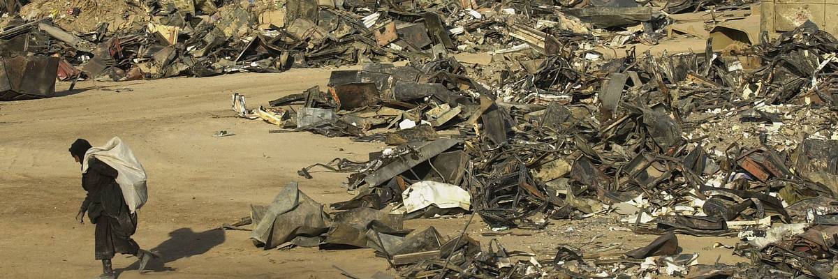 An Iraqi scrap dealer carries a bag a away from a pile of discarded military equipment.