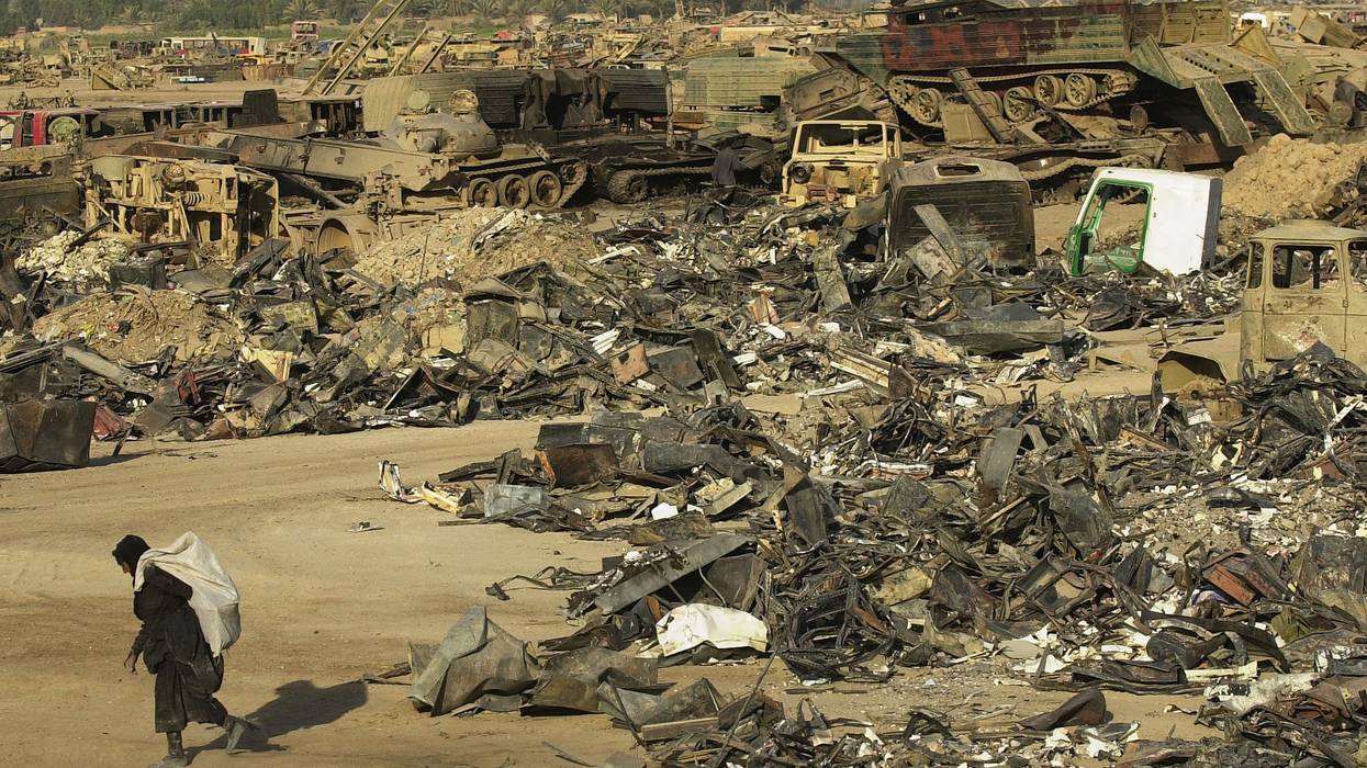 An Iraqi scrap dealer carries a bag a away from a pile of discarded military equipment.