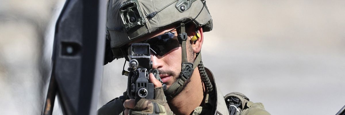 An Israeli soldier takes aim from behind a vehicle