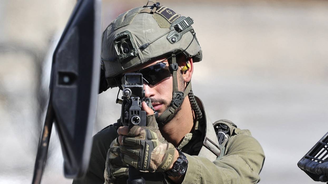 An Israeli soldier takes aim from behind a vehicle
