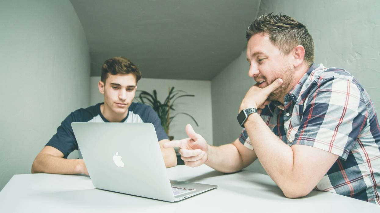 An older man points at a laptop while a younger man looks on.