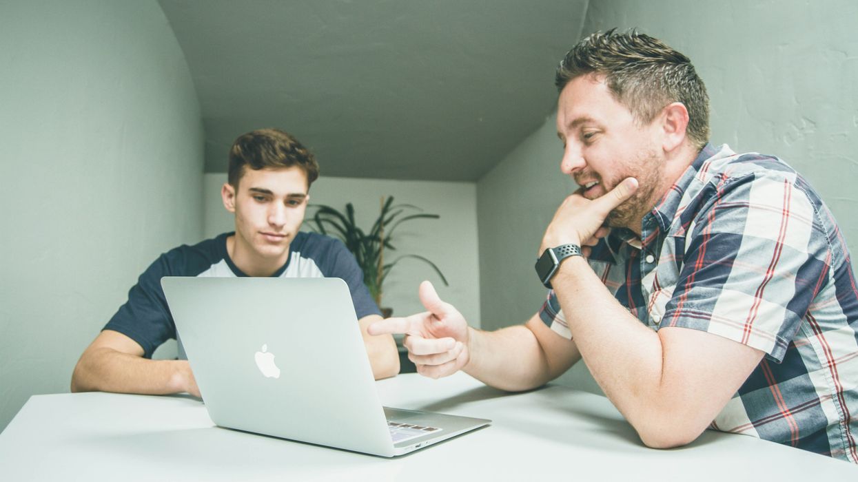 An older man points at a laptop while a younger man looks on.