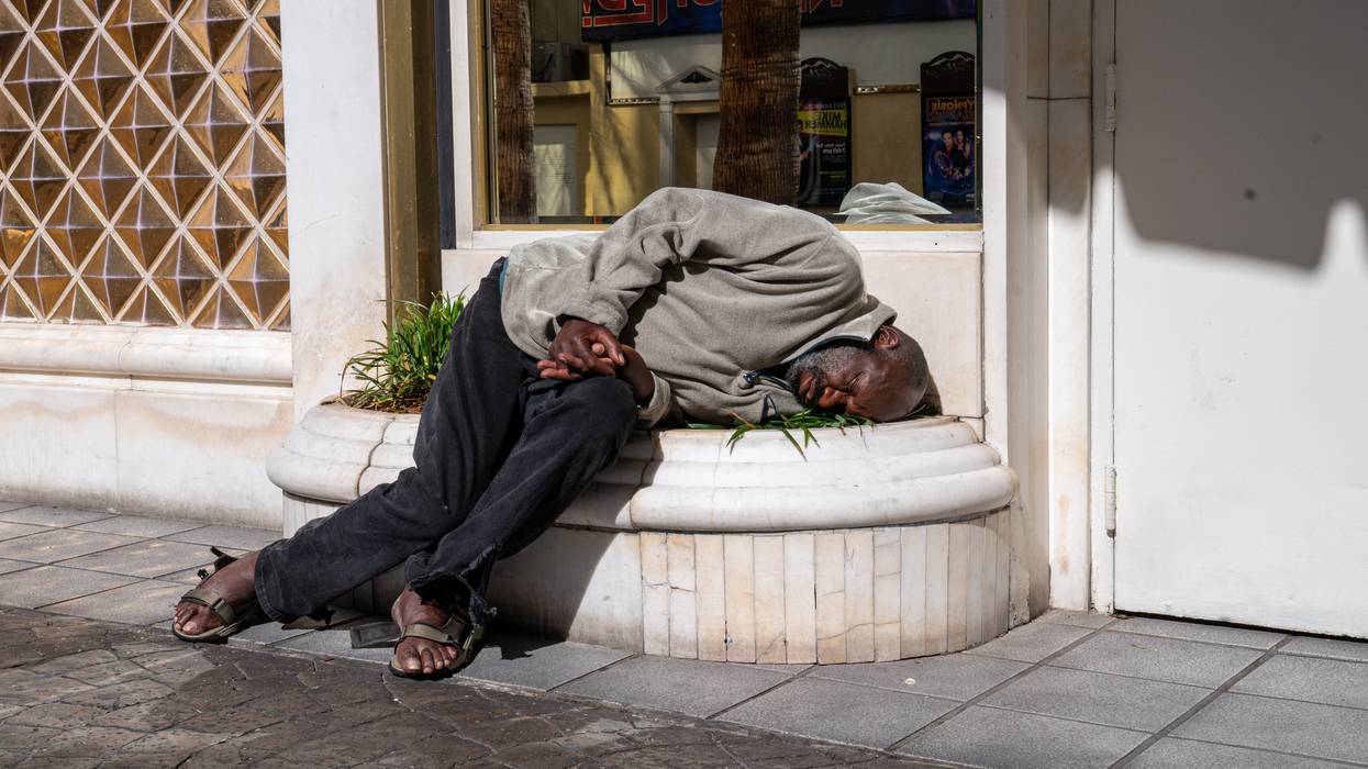 An unhoused man sleeps on a sidewalk