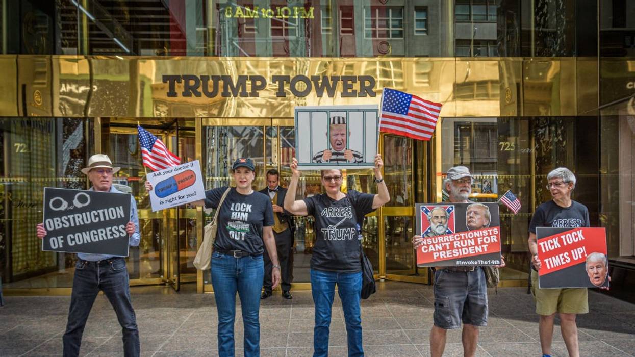 Anti-Trump protesters stand with signs in front of Trump Tower.