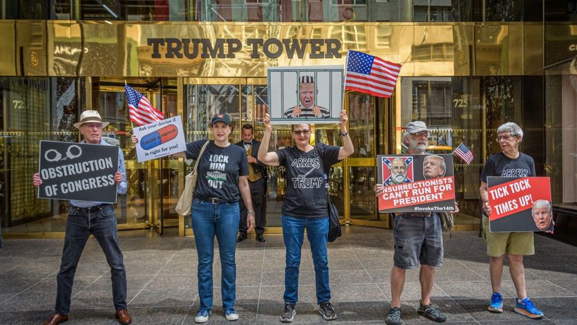 Anti-Trump protesters stand with signs in front of Trump Tower.