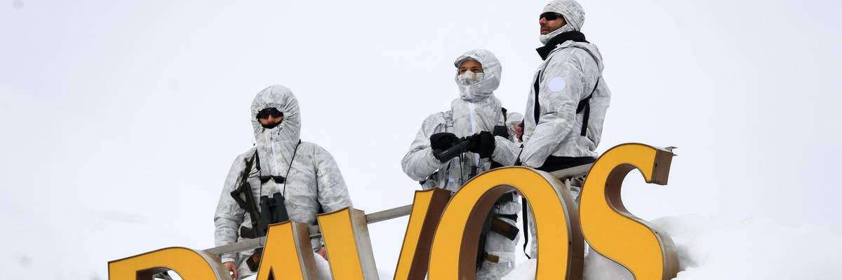 Armed security personnel stand guard on the rooftop of a hotel, next to letters reading "Davos"