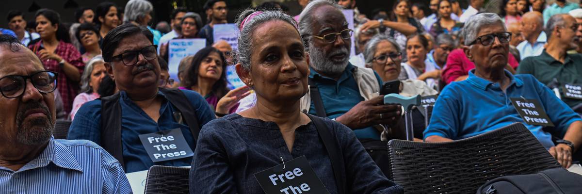 Arundhati Roy attends a demonstration wearing a small "Free the Press" sign.