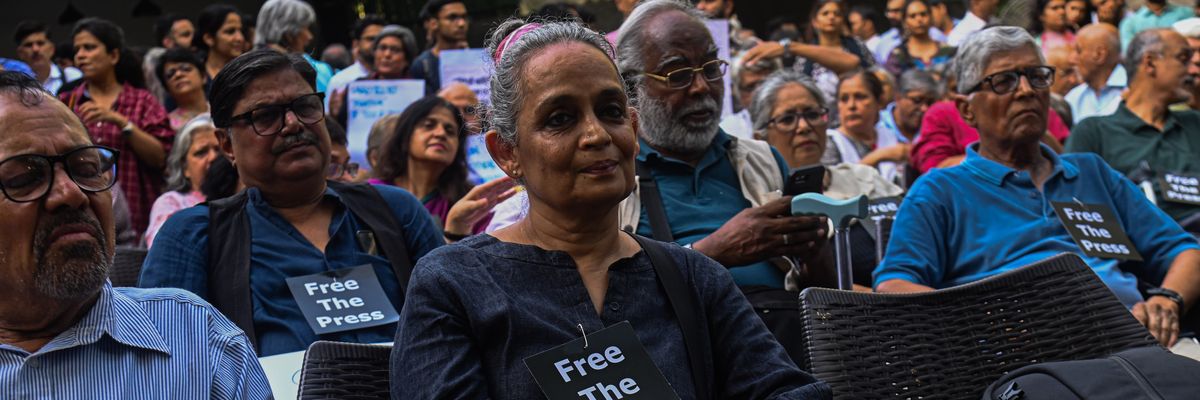 Arundhati Roy attends a demonstration wearing a small "Free the Press" sign.