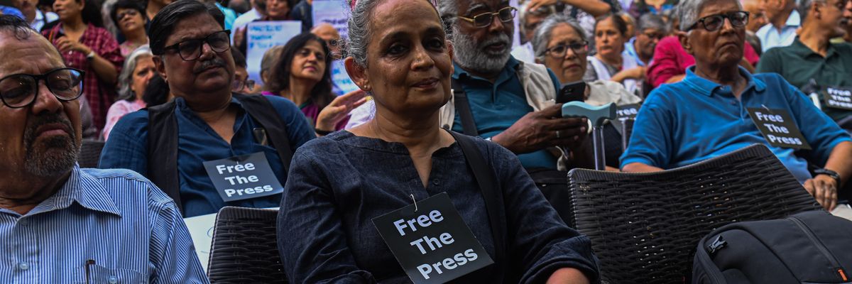 Arundhati Roy attends a demonstration wearing a small "Free the Press" sign.