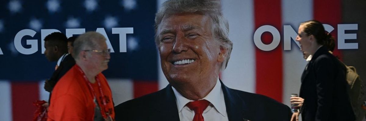 Attendees walk past large banner of Trump at first day of Republican National Convention