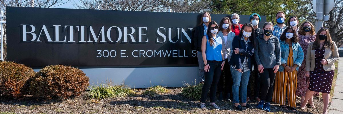 Baltimore Sun staff pose in front of the Sun sign.