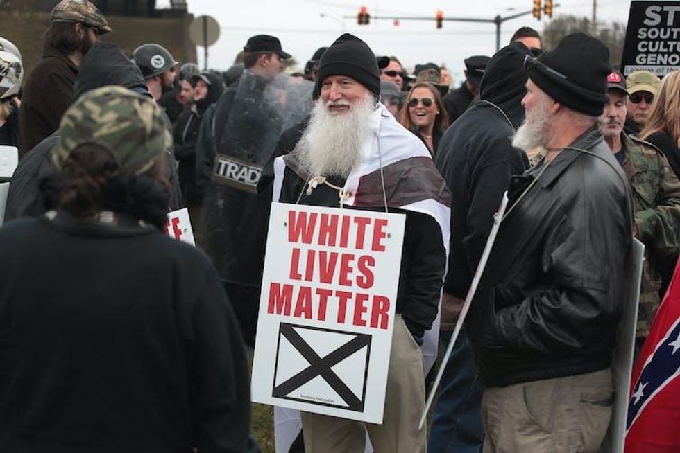 Bearded older man at a white supremacist rally carrying a sign that says 'White Lives Matter'