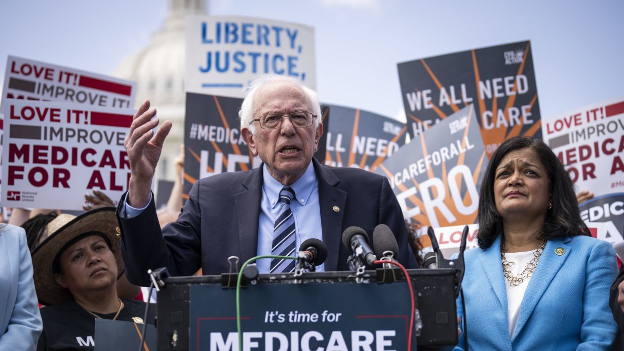 Bernie Sanders and Pramila Jayapal stand at a podium in front of signs.